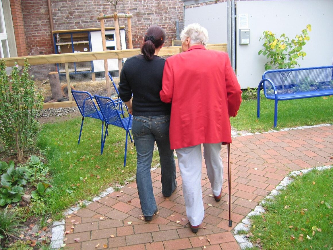 Pflegebedürftiger Mensch mit Angehöriger und Pflegekraft im Wohnzimmer